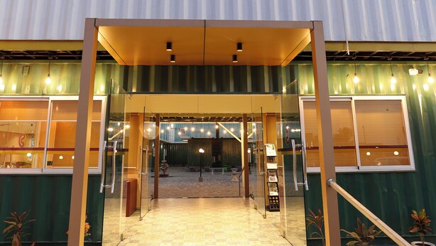 Het exterieur van Click Hotels, met een modern ontwerp, toont een opvallend neonbord, een glazen entree en een betegeld entreegebied.
