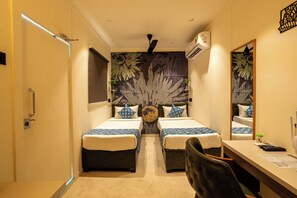 A compact hotel room with two single beds, a desk with a chair, a large mirror, and a decorative wall with a leaf pattern. - Click Hotel (Mundra)
