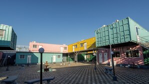 Een binnenplaats met in een patroon geplaatste zeecontainers, banken en een betegelde vloer.