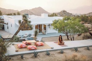 Un bâtiment moderne de couleur blanche, doté d’un patio aménagé avec des sièges extérieurs et un tapis de yoga.