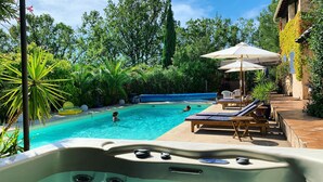 A swimming pool with lounge chairs and umbrellas, surrounded by lush greenery and a hot tub. - Chambre D'hôtes et Petit Déjeuner D'exceptionnel (Tourrettes)