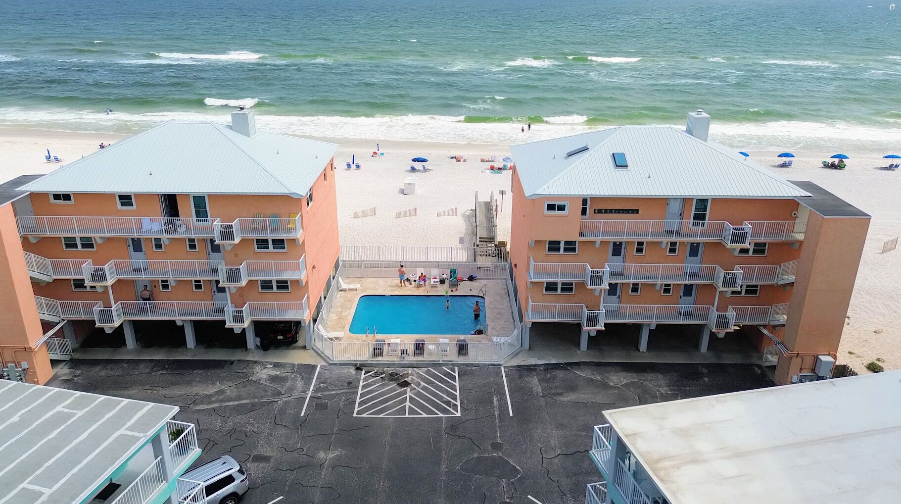 Un hôtel en bord de mer composé de deux bâtiments, doté d’une piscine centrale et offrant une vue sur la plage.