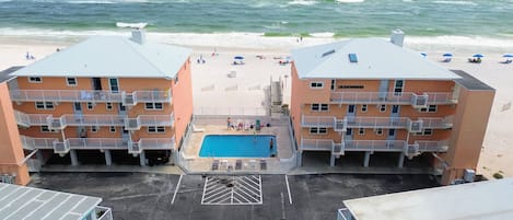 Un hôtel en bord de mer composé de deux bâtiments, doté d’une piscine centrale et offrant une vue sur la plage.
