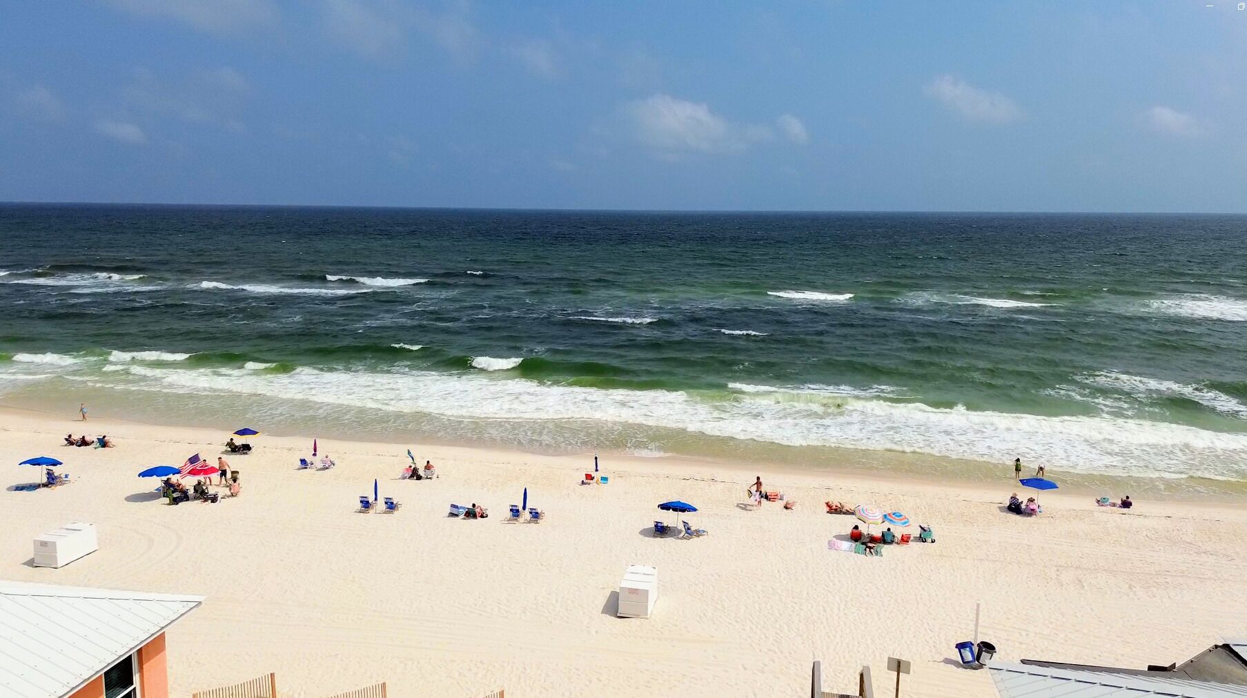 A beach with people relaxing under umbrellas, a lifeguard tower, and a clear view of the ocean.