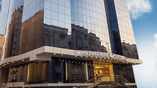 Ein modernes Hotel mit einer glänzenden Glasfassade, einem markanten Eingang und einem Schild mit der Aufschrift 'West Land Hotel'.