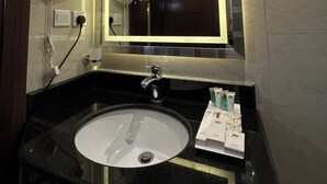 Ein Badezimmer mit einem schwarzen Waschbecken, einem Spiegel und einem Fön. Ein Schild ist an der Wand angebracht und eine Leuchte hängt über dem Spiegel.