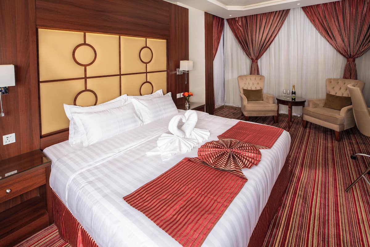 Una habitación de hotel con una cama grande, dos sillones, una mesita y una mesita de noche.