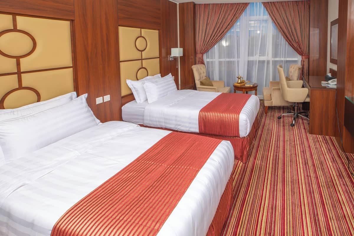 Habitación de hotel con dos camas, un escritorio, una silla y una ventana con cortinas.