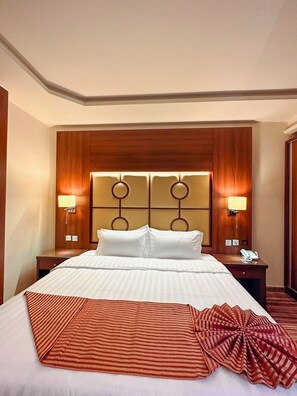 Habitación de hotel con una cama grande, dos mesitas de noche, un cabecero de madera y dos lámparas de pared.