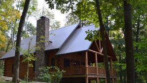 A log cabin with a stone chimney, wooden deck, and a large rock in front. - Find peace, tranquility and nature—secluded cabin on 42 acres with fishing pond (Warsaw)