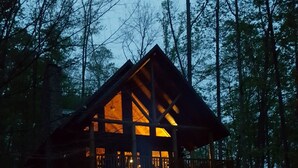 Una cabana amb una estança central espaiosa i una altra més petita a la planta superior, envoltada per un bosc.