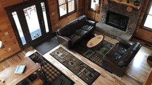 A cozy cabin-style room with a fireplace, wooden floors, a leather sofa, and a coffee table. - Find peace, tranquility and nature—secluded cabin on 42 acres with fishing pond (Warsaw)