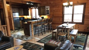A rustic cabin interior with a kitchen, dining area, and living room. - Find peace, tranquility and nature—secluded cabin on 42 acres with fishing pond (Warsaw)