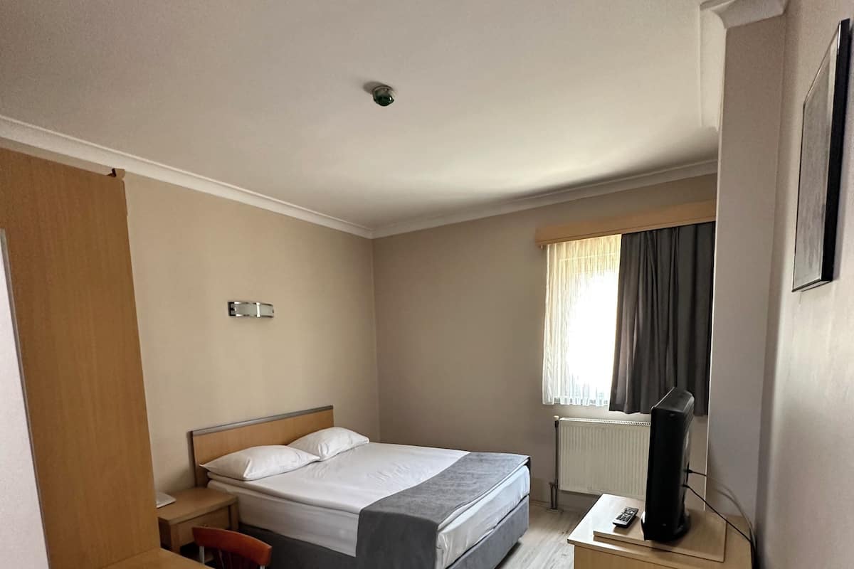 Una habitación de hotel con cama, escritorio, silla, televisor y ventana con cortinas.