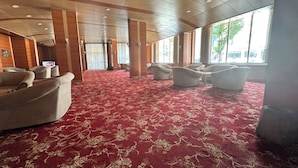 Amplia habitación con alfombra roja y varios sofás dispuestos para sentarse.