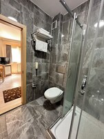A modern bathroom with a glass-enclosed shower, a toilet, and a towel rack.