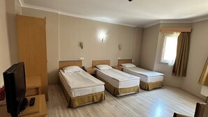 Habitación de hotel con tres camas, televisión, escritorio y una silla.