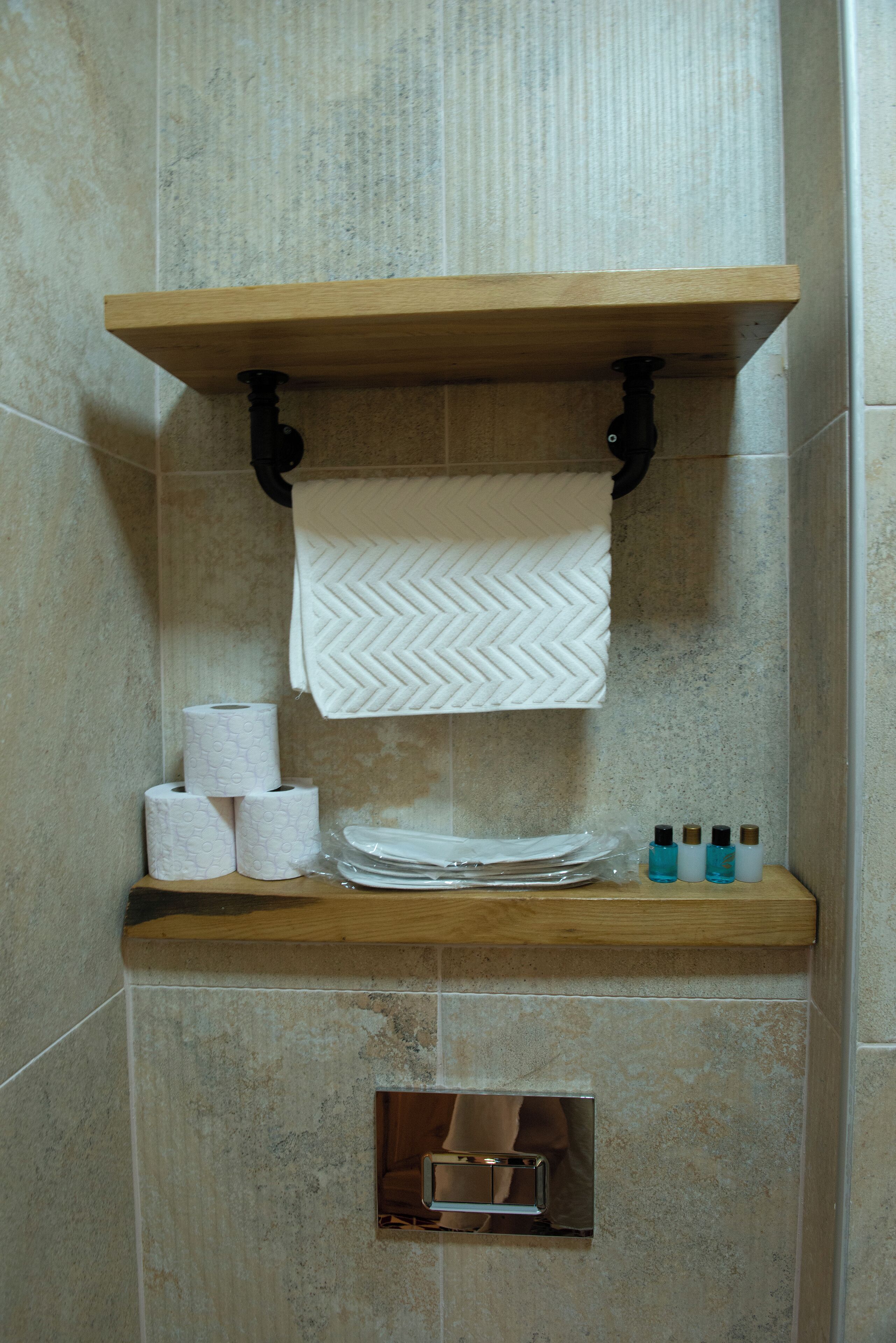 Casa de banho com uma estante de madeira contendo papel higiénico, uma toalha e artigos de higiene pessoal.