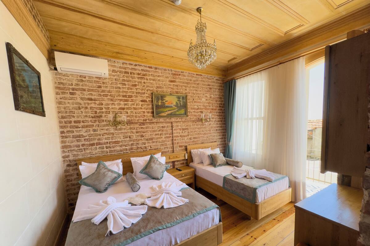 Ein Zimmer mit zwei Holzbetten, einer Backsteinwand, einer Kandelaber und einem Gemälde.