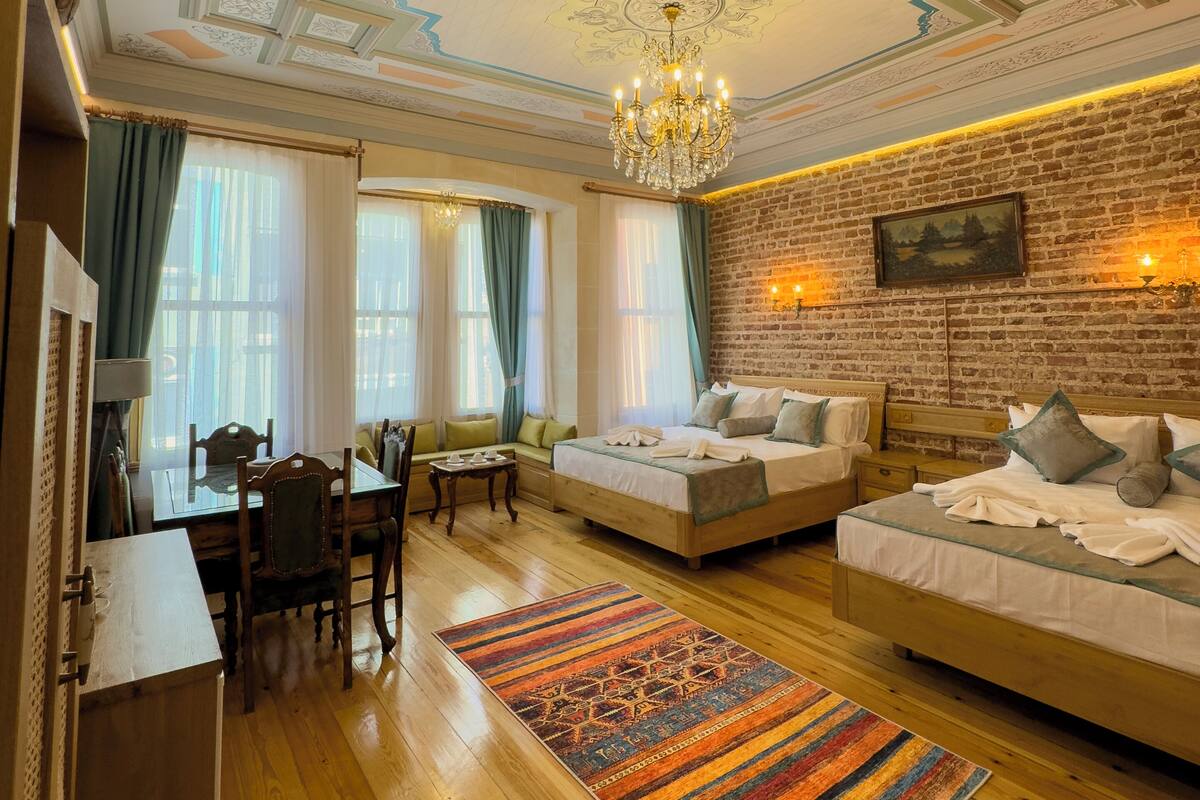 Ein Hotelzimmer mit Holzboden, einem farbenfrohen Teppich, einer Chandelier und einer Ziegelwand.