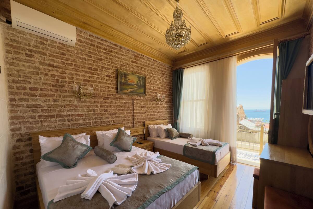 Ein Hotelzimmer mit zwei Betten, einer Ziegelwand, einer Kandelaber und Blick aufs Meer.