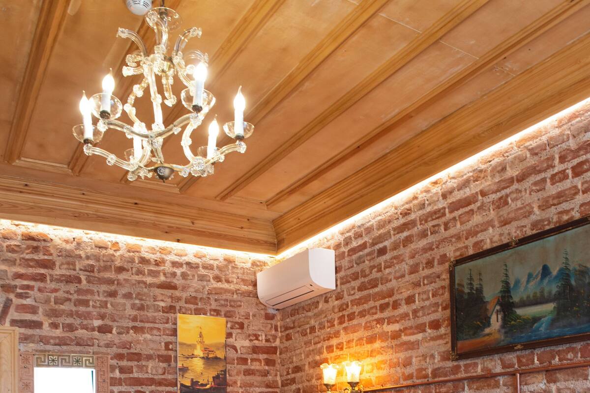 Ein Hotelzimmer mit Backsteinwand, Holzboden, zwei Betten mit weißen Leinen, einer Chandelüster, einem Gemälde und einer Wandlampe.