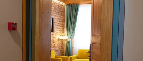 A hallway leading to a room with a brick wall, yellow chairs, a wooden ceiling, and a patterned rug.