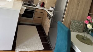 Een moderne keuken met houten kastjes, een roestvrijstalen koelkast, een inbouwoven en een klein eetgedeelte met een blauwe stoel en een tafel.