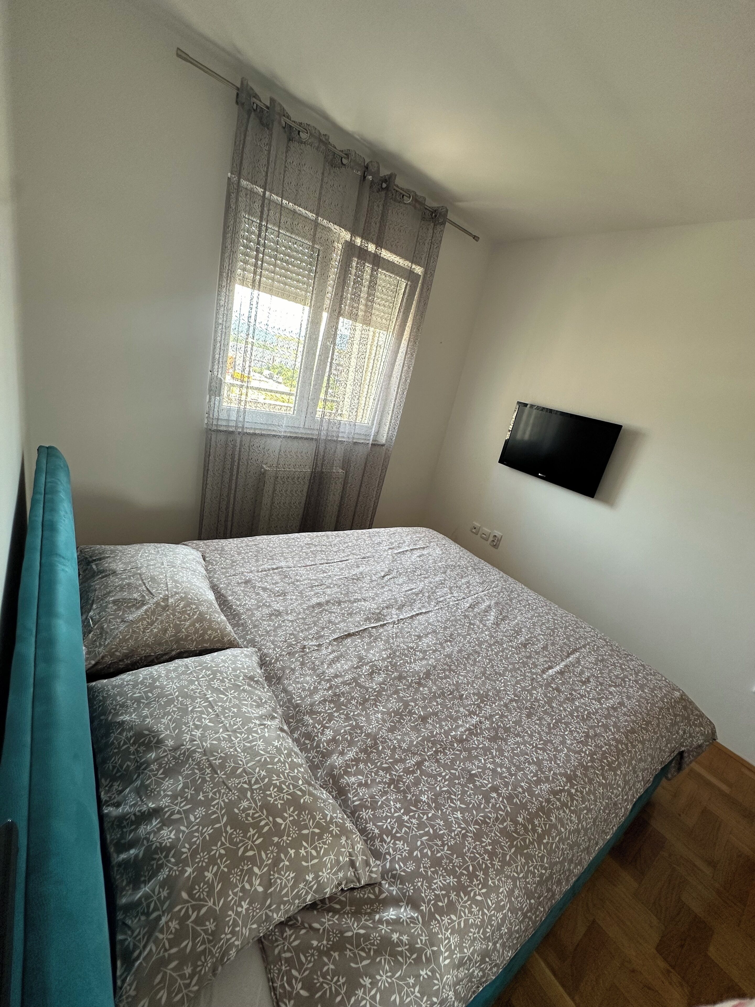 Un dormitorio con una cama, un televisor montado en la pared y un ventanal con cortinas.