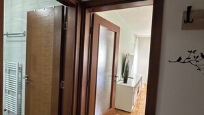 Een gang met een houten deur die leidt naar een kamer met een wit aanrecht en een potplant.