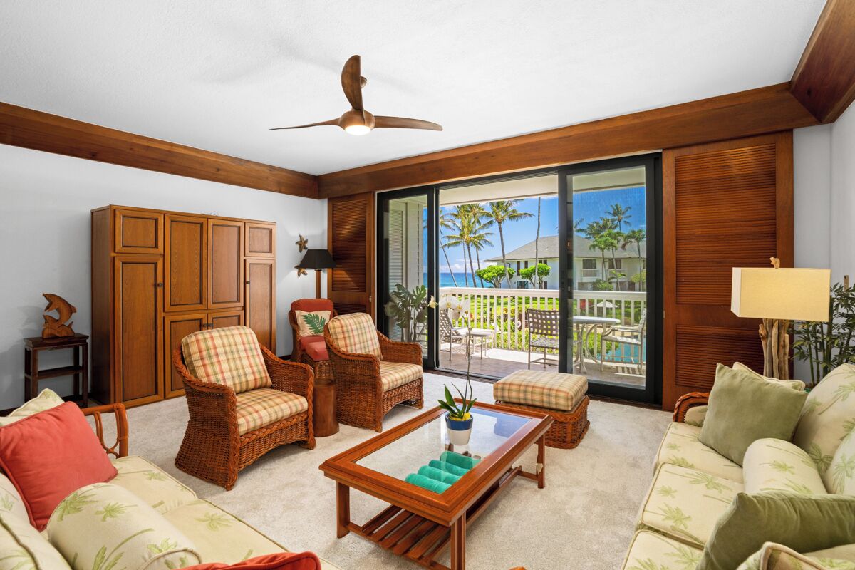 Un ampio soggiorno con mobili in vimini, una ventola a soffitto e vista su un paesaggio tropicale attraverso grandi porte scorrevoli.