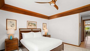 Un dormitorio con una cama de madera, dos mesitas de noche, un ventilador de techo y cuadros en las paredes.
