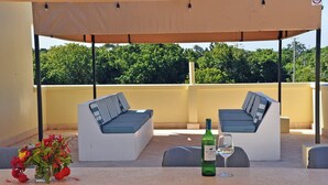 A rooftop terrace with two white sofas, a table with a bottle of El Chivo wine and a glass, and a vase of flowers. - Cozy studio in peaceful Diani located in a leafy and serene neighborhood (Diani)