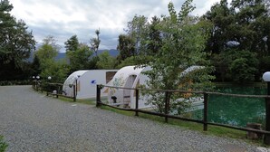 A row of white RVs with a logo, set against a backdrop of trees and a lake. - FLOATING DREAM (Fiano)