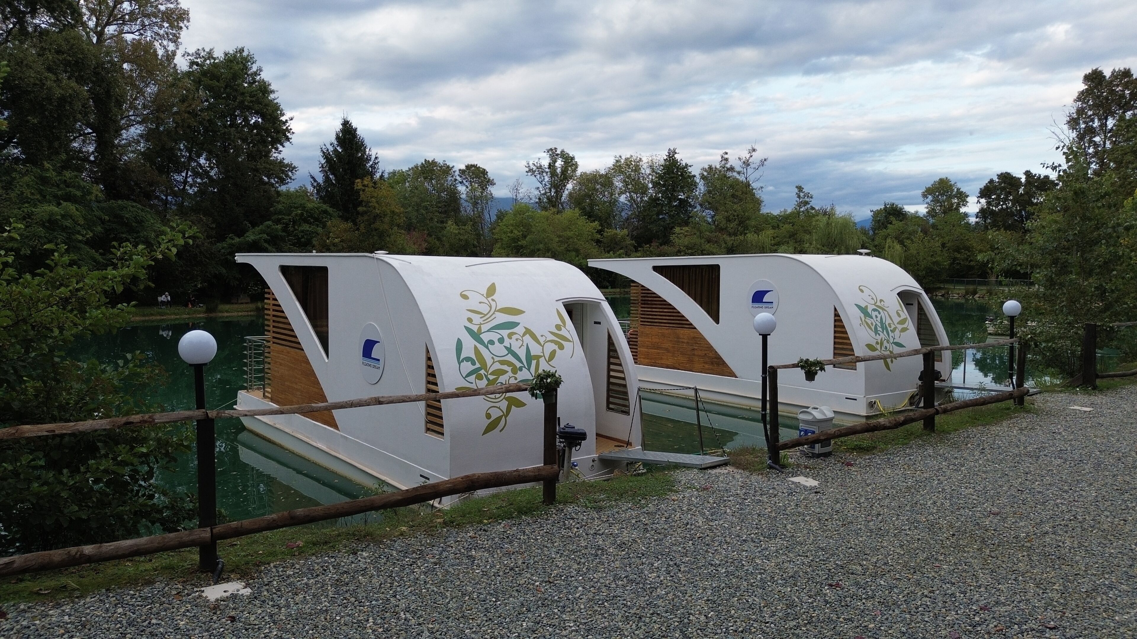 Two floating cabins with a logo, a wooden deck, and a view of a lake surrounded by trees.