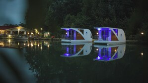 Two modern, illuminated houseboats on a calm body of water, reflecting the lights. - FLOATING DREAM (Fiano)