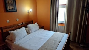 Een net opgemaakt bed met witte lakens in een kamer met oranje wanden, een lijst met een afbeelding en een nachtkastje met een lamp.