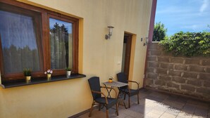 A small outdoor seating area with a table and two chairs, a window with a view of trees, and a potted plant on the windowsill. - Radio Hotel Bratislava (Bratislava)