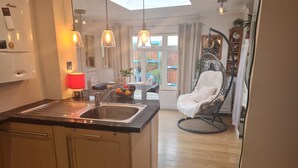 Een moderne keuken met een centraal eiland, hangende verlichting en uitzicht op de eetruimte.