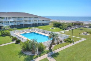 A hotel with a swimming pool, a beach view, and a covered pavilion.