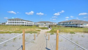 Ein Hotel direkt am Strand mit mehreren Gebäuden, einem Sandweg zum Eingang und blauem Himmel.