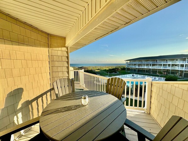 A balcony with a table and chairs, overlooking a beach and a resort building. - SSV 205 - Sunshine Oasis: Oceanfront condo in Oak Island, sleeps 8 with pool access! (Oak Island)