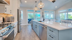 A modern kitchen with stainless steel appliances, a large island, and pendant lighting. - Slow n Steady: Swim Spa, Elevator, Beach Walk (Oak Island)