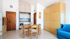 A compact kitchen with wooden cabinets, a dining table with chairs, a blue sofa, and a wardrobe. - Corallo Blu in San Teodoro (San Teodoro)