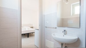A modern bathroom with a white sink, a mirror, and a bedside table with a white towel. - Das Halte Haus - Room 302 (Olbia)