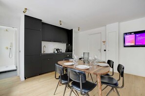 Een moderne keuken met donkere kastjes, een eettafel voor zes personen en een flatscreen televisie aan de muur.
