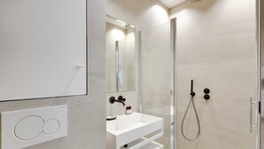 Un baño moderno con ducha de vidrio, lavabo blanco y un espejo grande.
