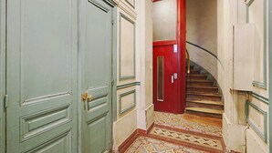Un pasillo estrecho con una puerta verde a la izquierda y una roja a la derecha, que conduce a una escalera.