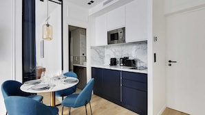 A modern kitchen with dark blue cabinets, a white countertop, and a built-in microwave. There is a dining area with blue chairs and a round table set for four.