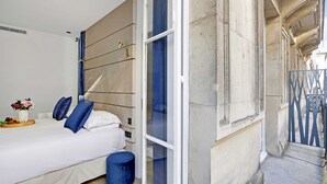 A bedroom with a bed, a bedside table with a vase, and a window with a view of the street.